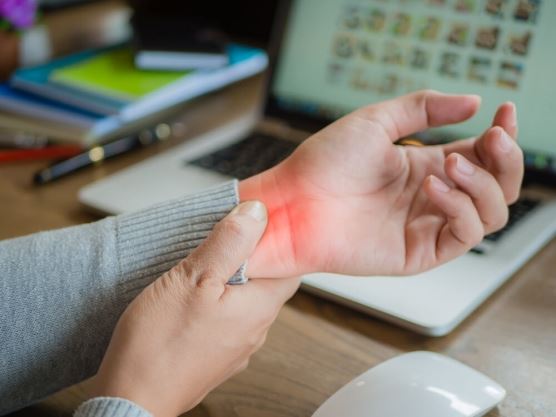 closeup of person behind laptop grabbing wrist from carpal tunnel pain